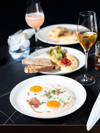 Elegantes Fr&uuml;hst&uuml;ck bei WILMA mit Spiegelei, Speck, Hummus, Brot und spritzigen Getr&auml;nken.