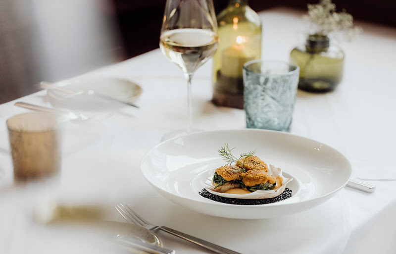 Elegant angerichtete, gratinierte Jakobsmuschel begleitet von einem exklusiven Wei&szlig;wein im Restaurant der Stasta.