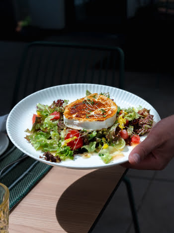 Ein Kellner bringt einen gegrillten K&auml;se auf Salat zum Tisch.