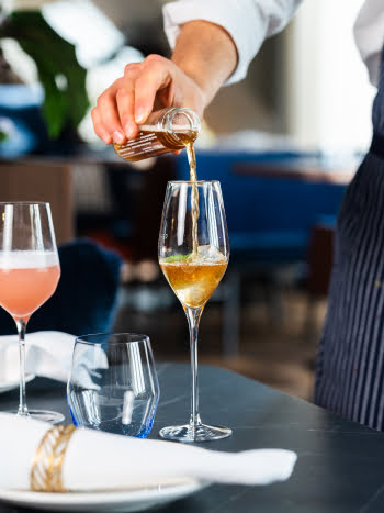 Ein Kellner schenkt Sine Vino Verjus Traube Isabella über Eiswürfel in ein hohes Glas ein.